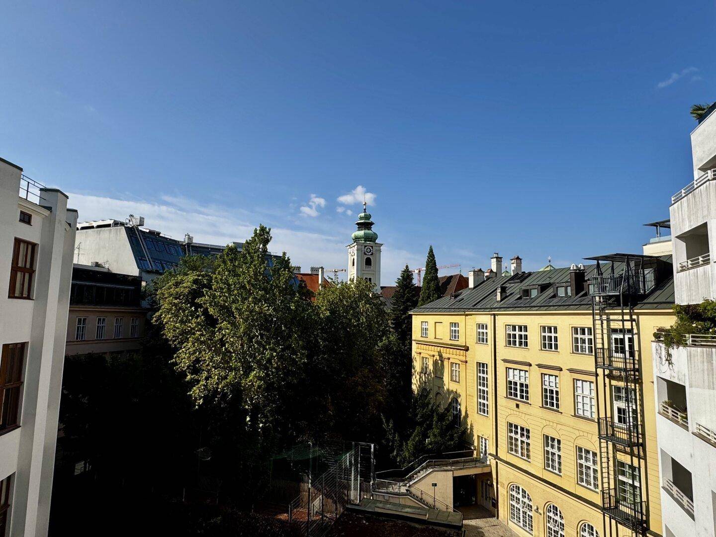 Panoramablick auf die Stadt mit historischen Gebäuden und einem Kirchturm unter blauem Himmel.