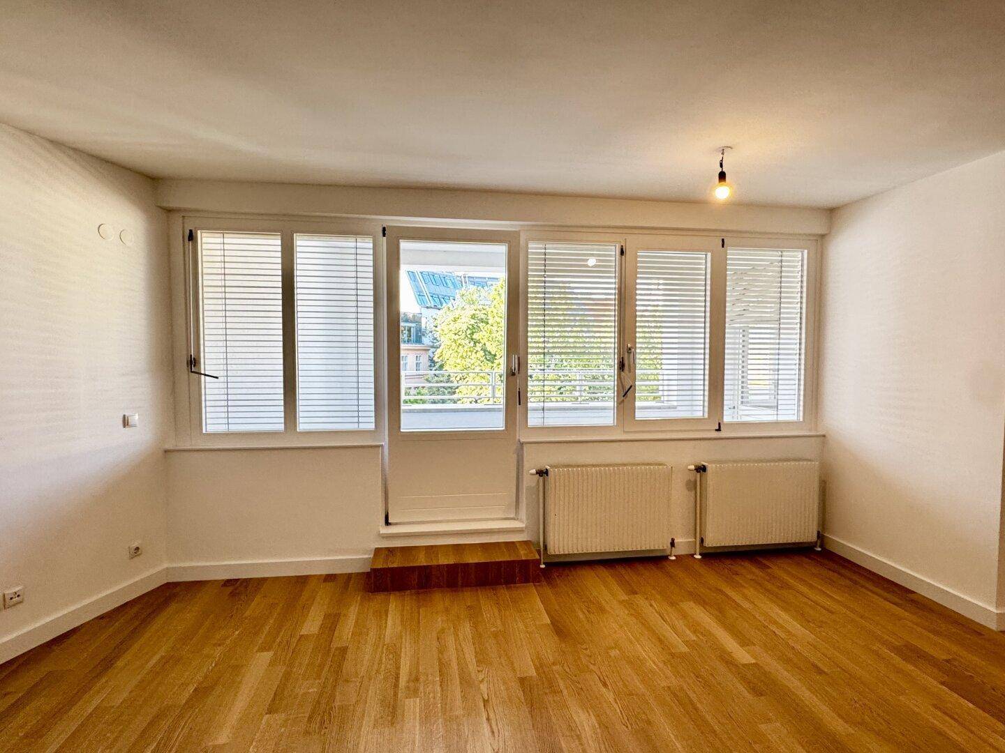 Helles Wohnzimmer mit Parkettboden, großen Fenstern und Zugang zu einem Außenbereich.