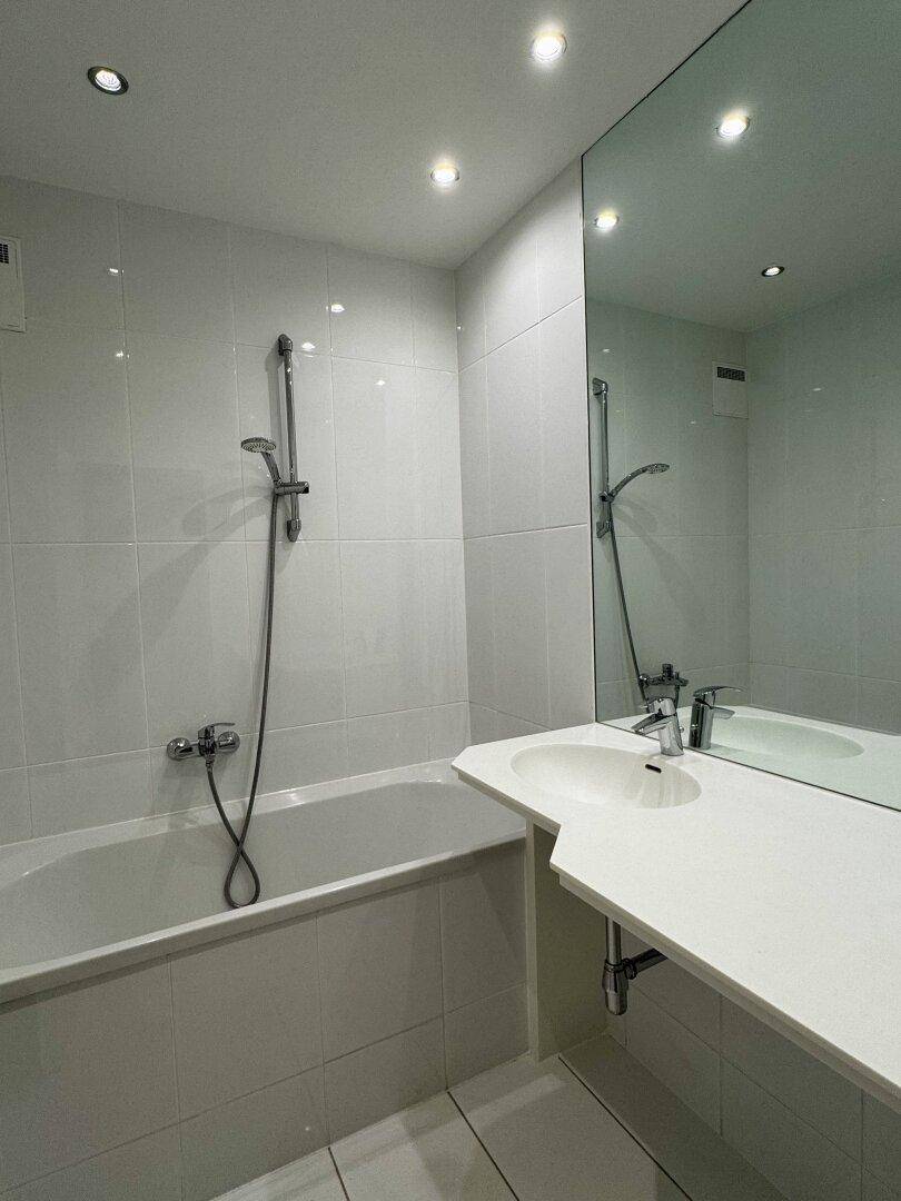 Modernes Badezimmer mit Badewanne, integriertem Waschbecken und großem Spiegel.
