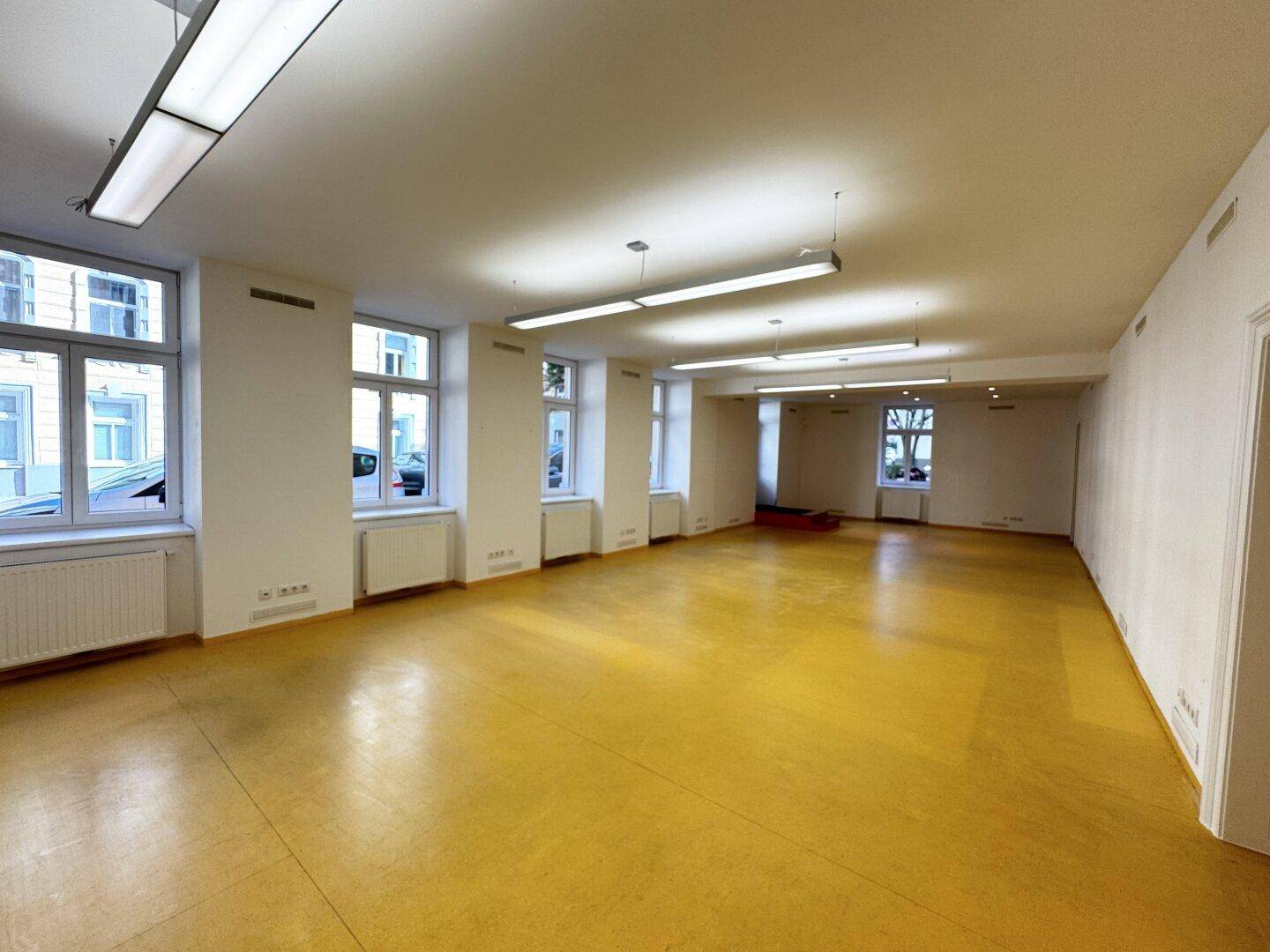 Heller und geräumiger Bürobereich mit vielen Fenstern und gelbem Bodenbelag.