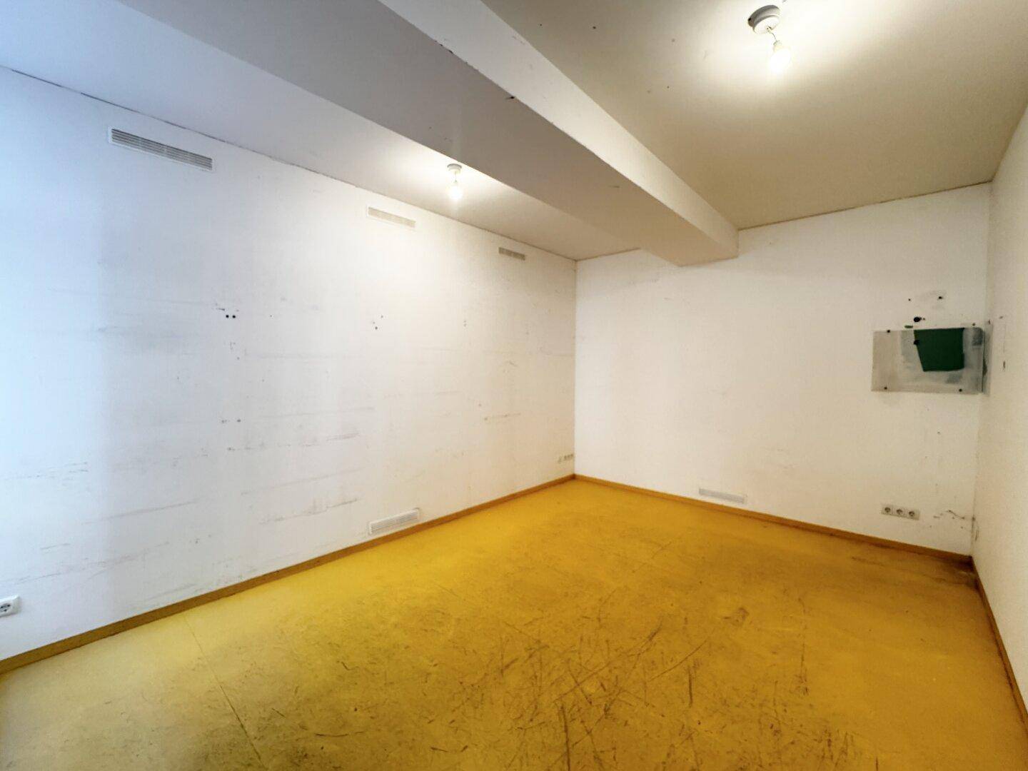 Kleiner, leerer Raum mit gelbem Boden und weißen Wänden, möglicherweise als Lagerraum nutzbar.