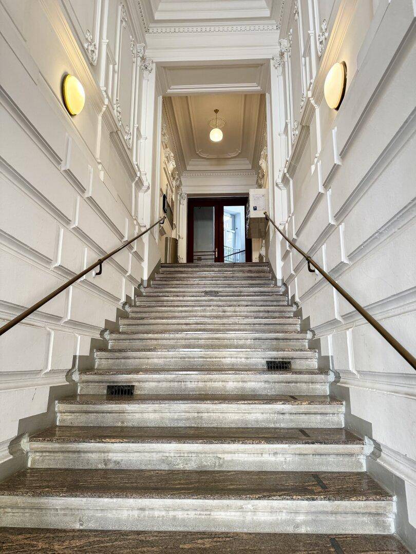 Elegantes Treppenhaus mit Marmorstufen, verzierten Wänden und klassischer Beleuchtung.