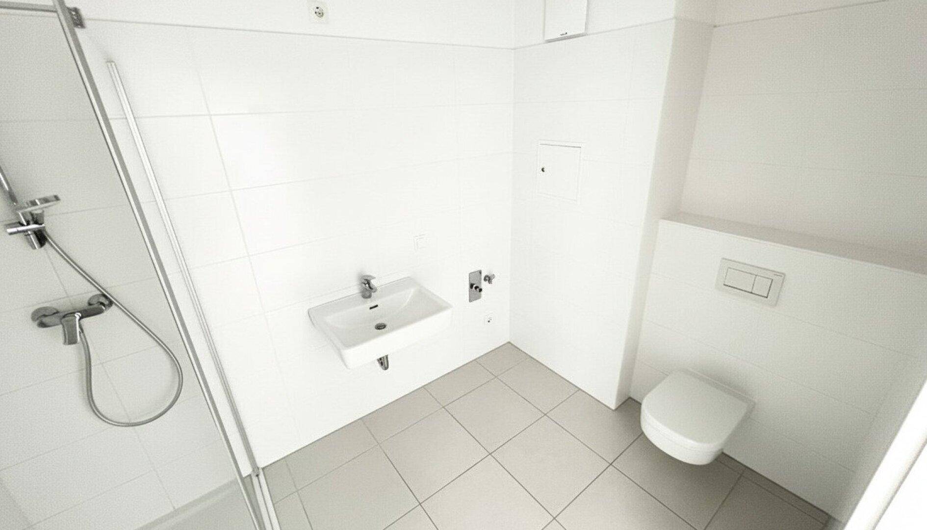 Modernes Badezimmer mit weißen Fliesen, einer Dusche und wandhängendem WC und Waschbecken.