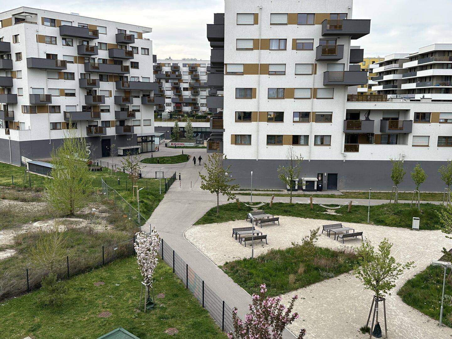 Moderne Wohnanlage mit mehreren Gebäuden, Grünflächen und Wegen in einer städtischen Umgebung.