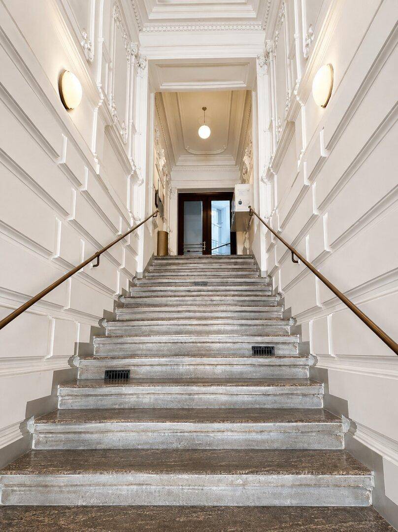 Elegantes Treppenhaus mit Marmorstufen, verzierten Wänden und klassischem Geländer in einem Altbau.