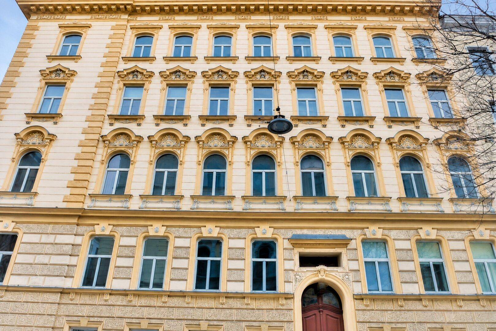 Prächtige Altbaufassade mit vielen Fenstern und dekorativen Elementen in hellem Gelbton.
