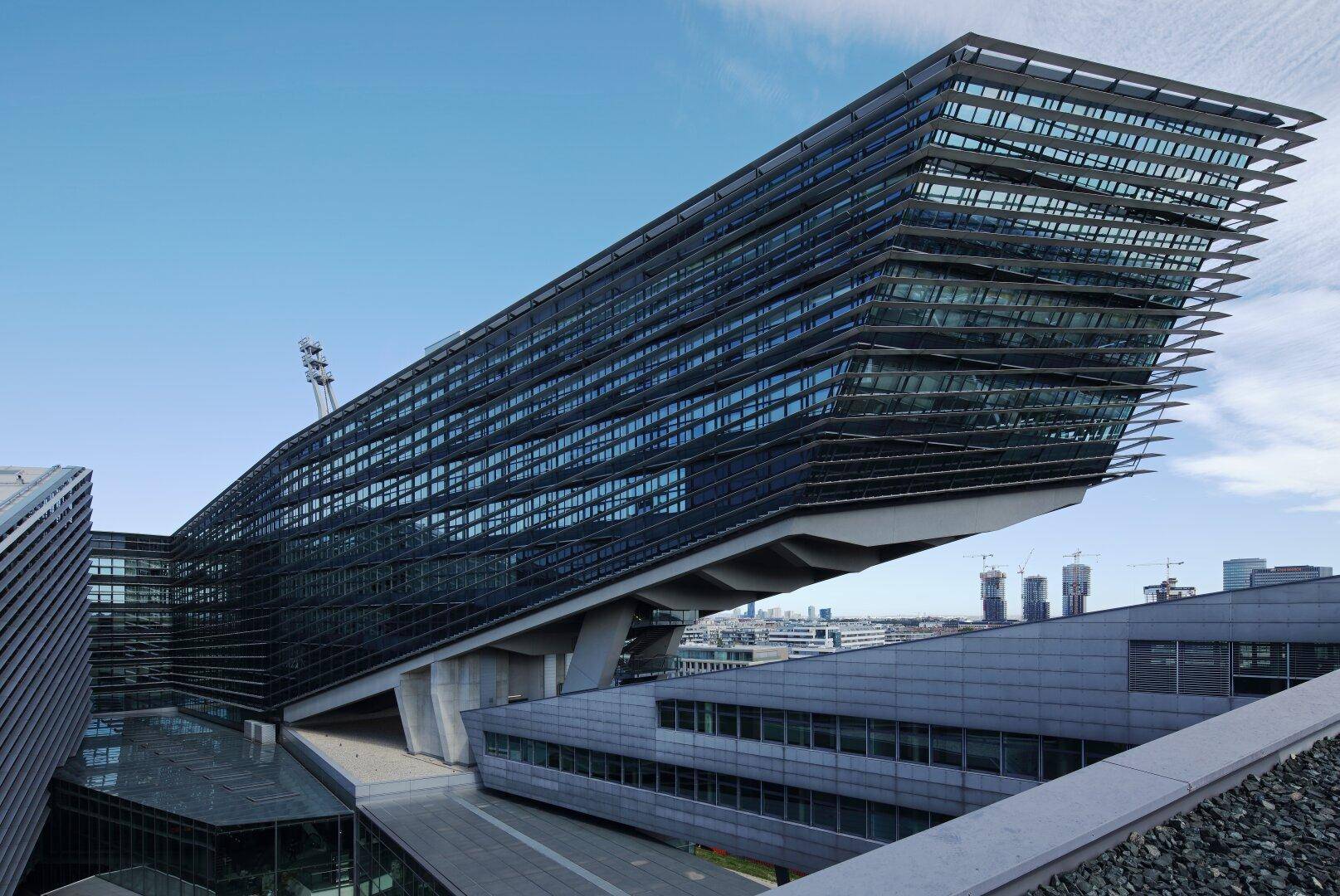 Auffälliges, modernes Bürogebäude mit schräger Glasfassade und komplexer Architektur unter blauem Himmel.