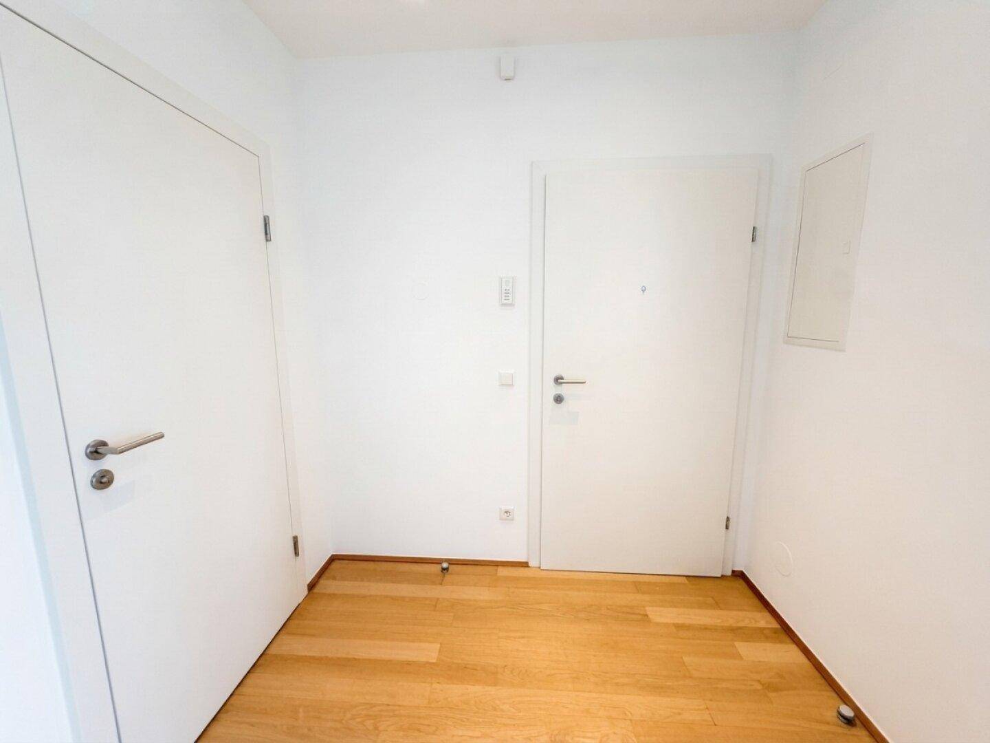 Heller Eingangsbereich mit Holzboden und weißen Türen, die zu verschiedenen Räumen führen.