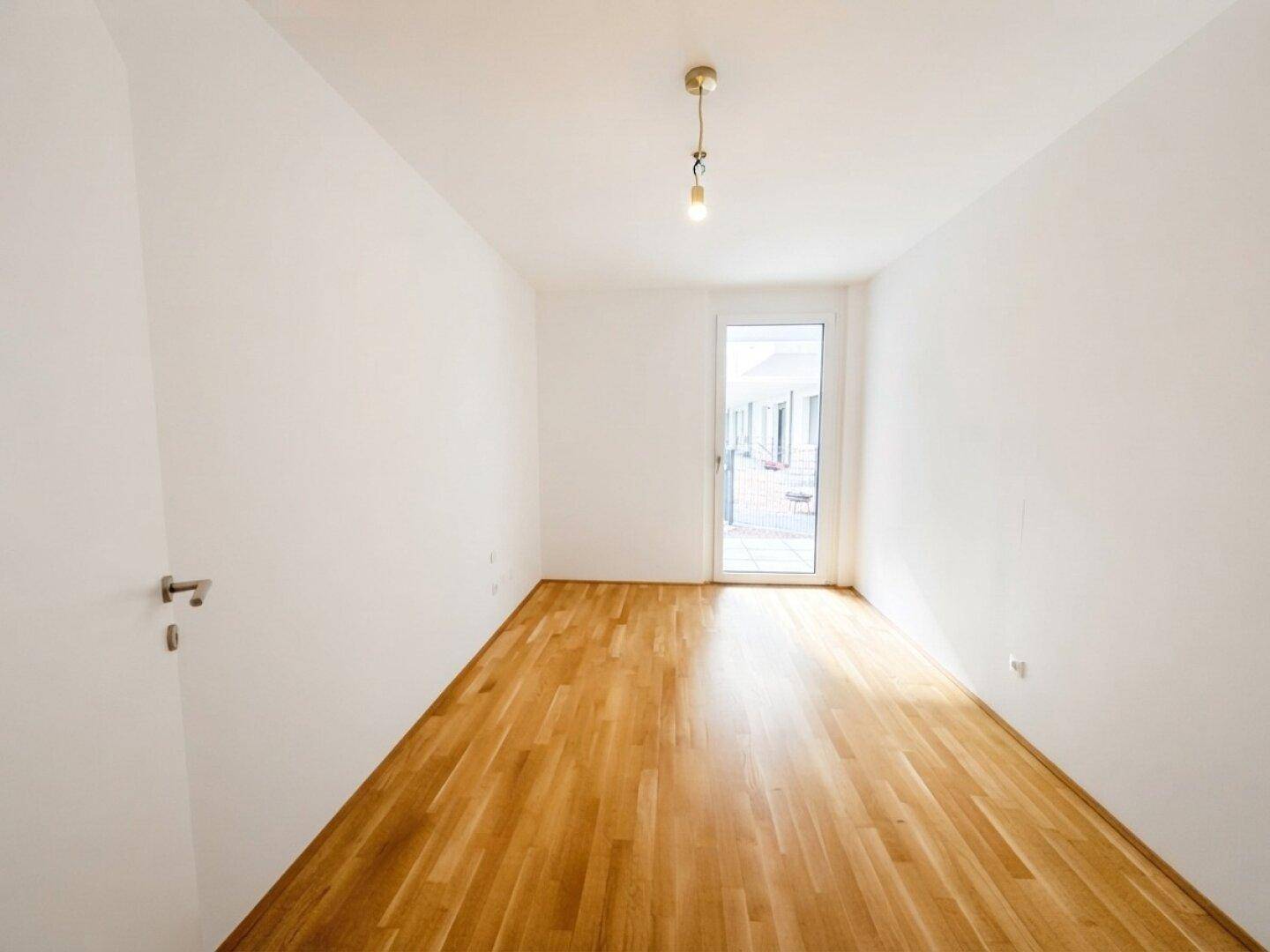 Helles Schlafzimmer oder Arbeitszimmer mit Parkettboden und Zugang zu einem Außenbereich.