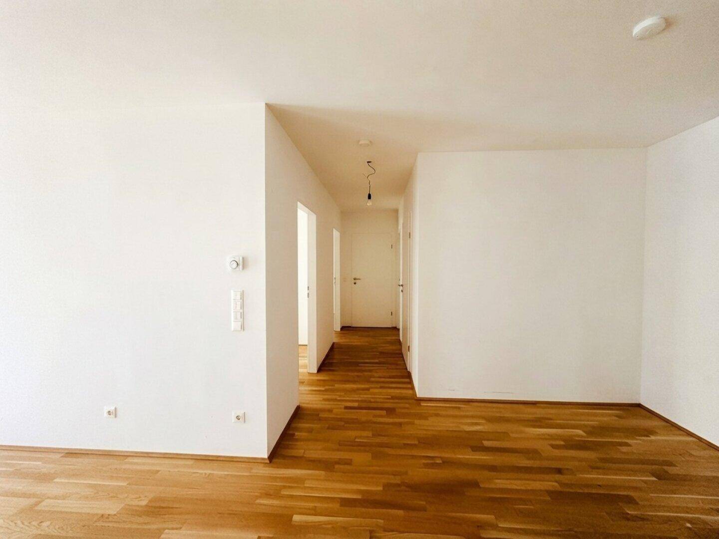 Offener Wohnbereich mit Parkettboden, der in einen hellen Flur übergeht.