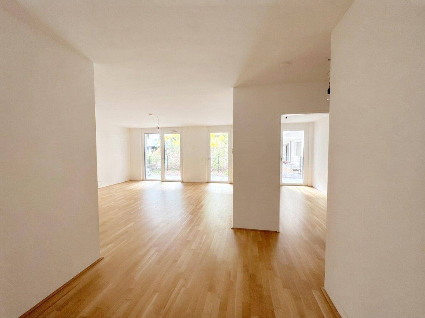 Großzügiger, lichtdurchfluteter Wohnbereich mit hellem Parkettboden und mehreren Zugängen nach draußen.