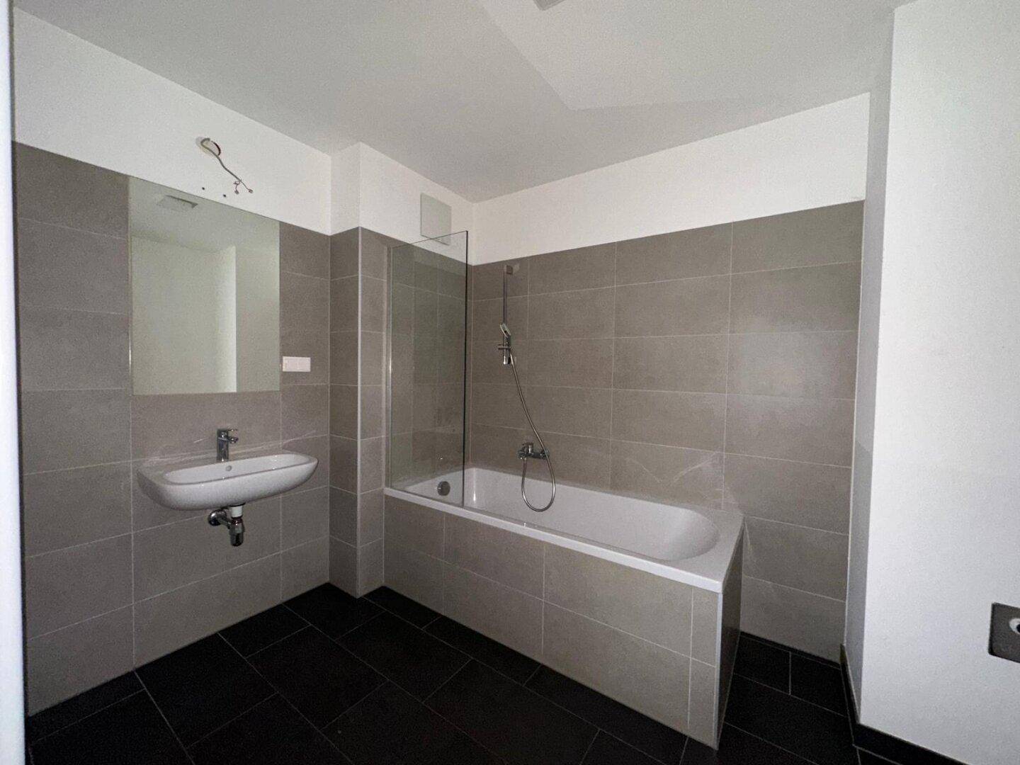 Modernes Badezimmer mit Badewanne, Einzelwaschbecken und grauen Wand- und Bodenfliesen.