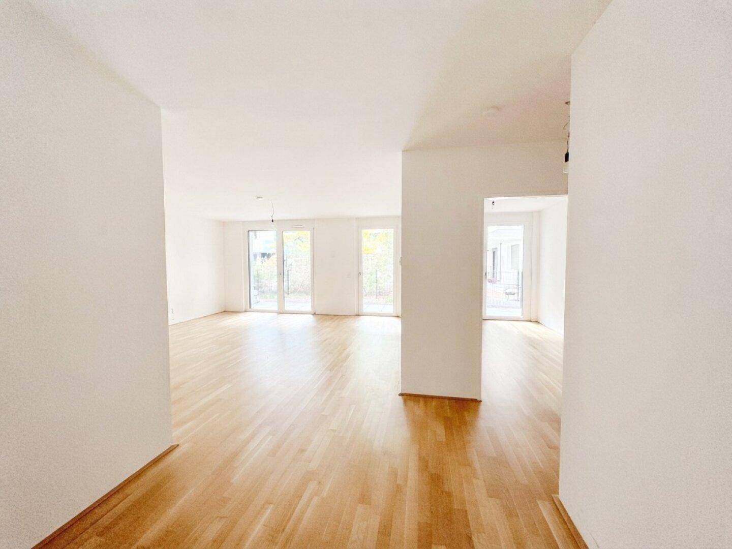 Geräumiger, heller Wohnbereich mit Parkettboden und mehreren Fenstertüren für viel Tageslicht.