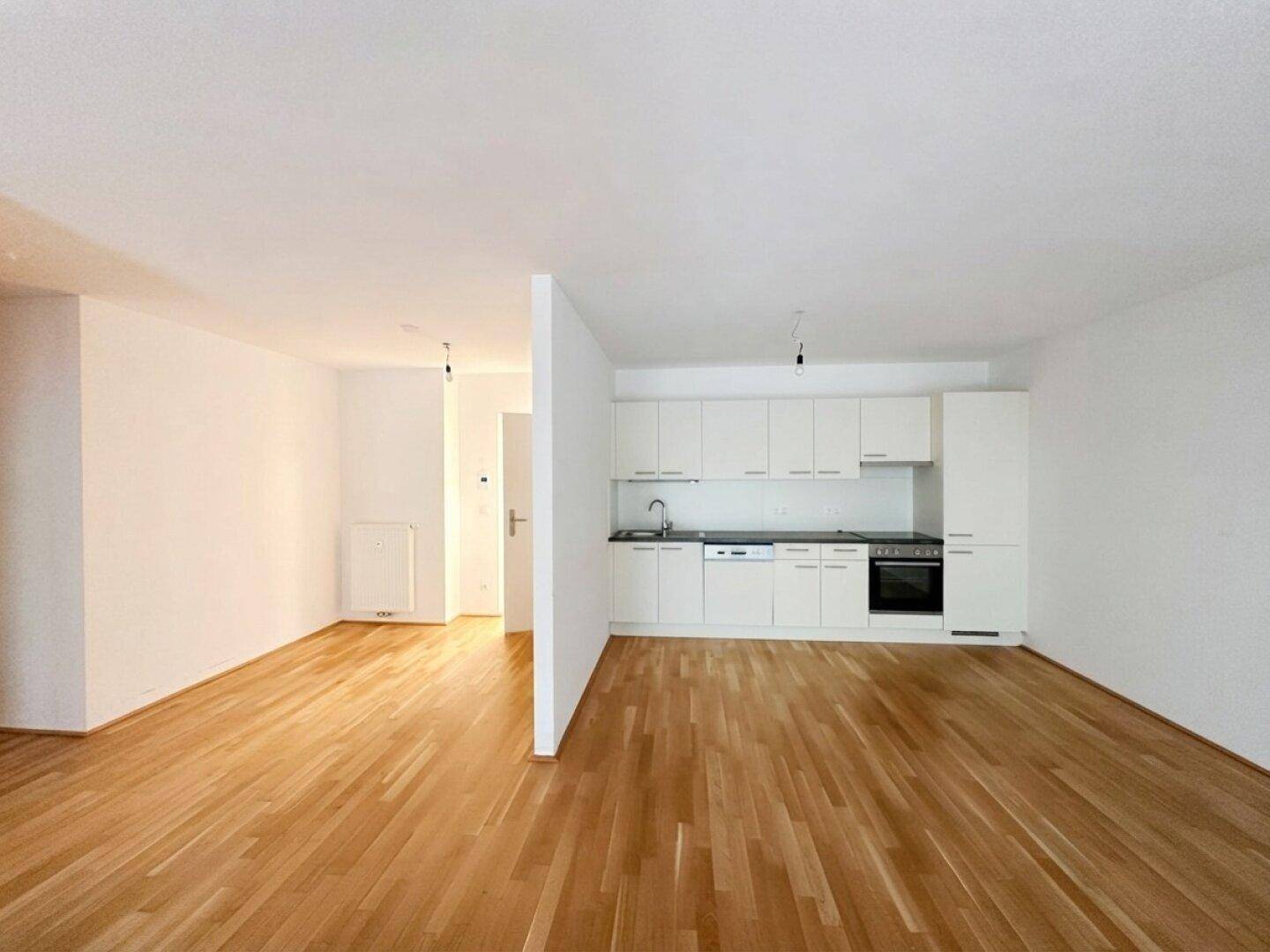 Offene Küche mit weißen Schränken, integrierten Geräten und Holzboden in einem hellen Raum.