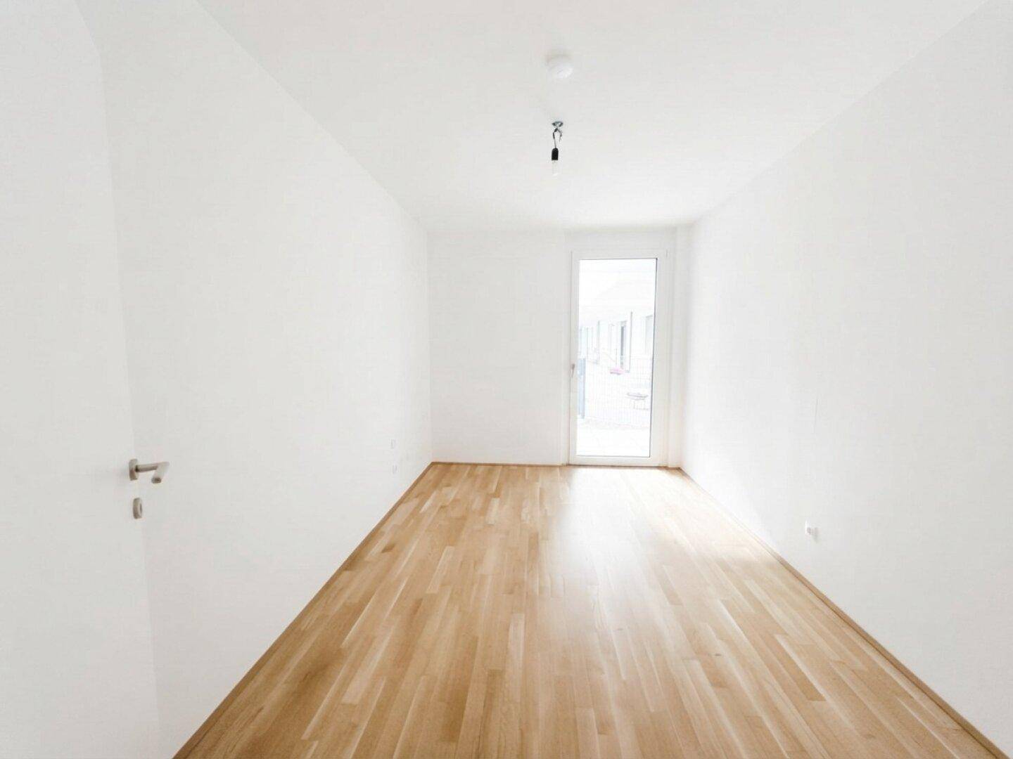 Helles Schlafzimmer mit Holzboden und einer Glastür, die viel natürliches Licht hereinlässt.