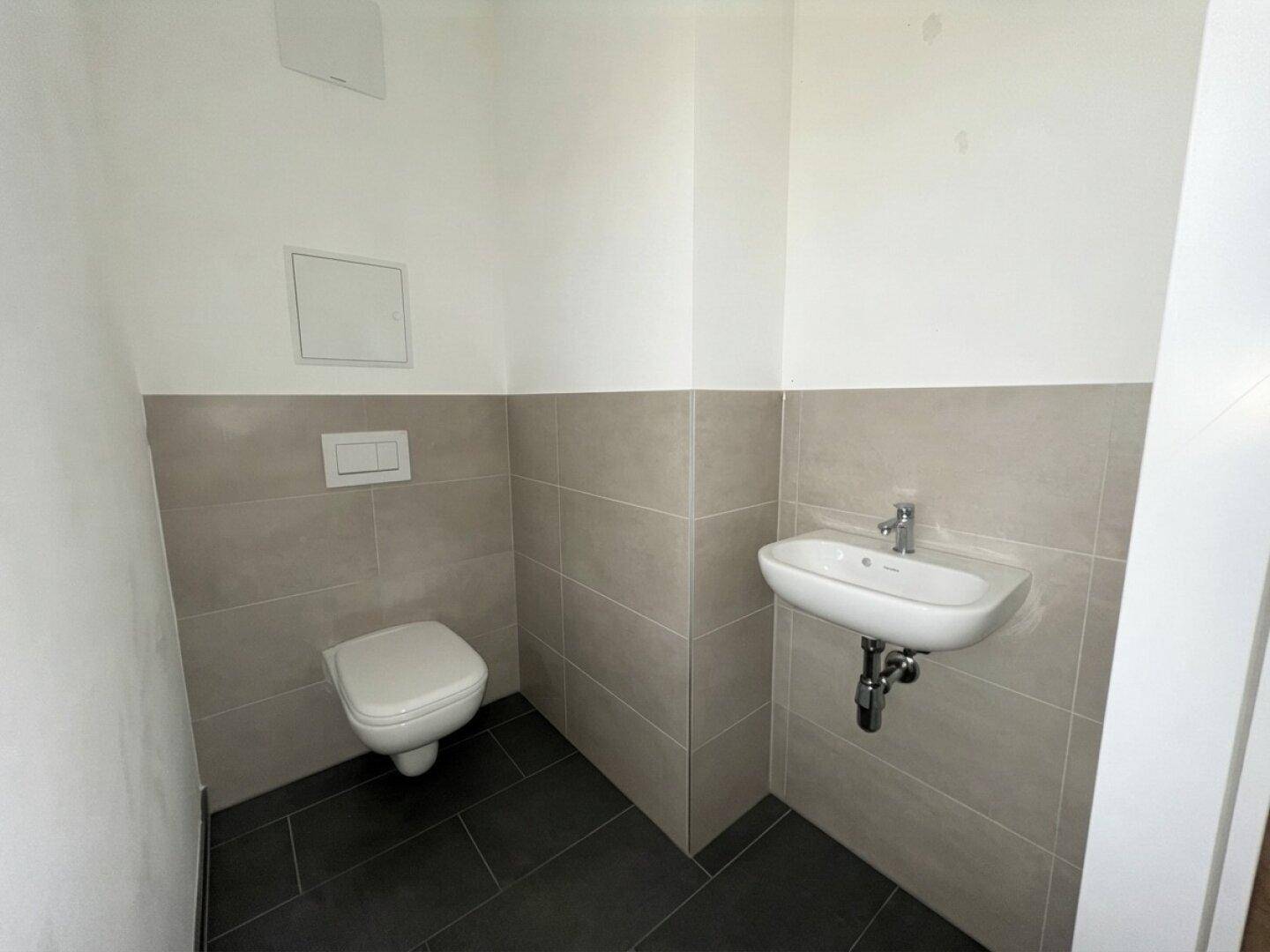 Modernes Gäste-WC mit Wand-WC, Einzelwaschbecken und grauen Fliesen an Wänden und Boden.