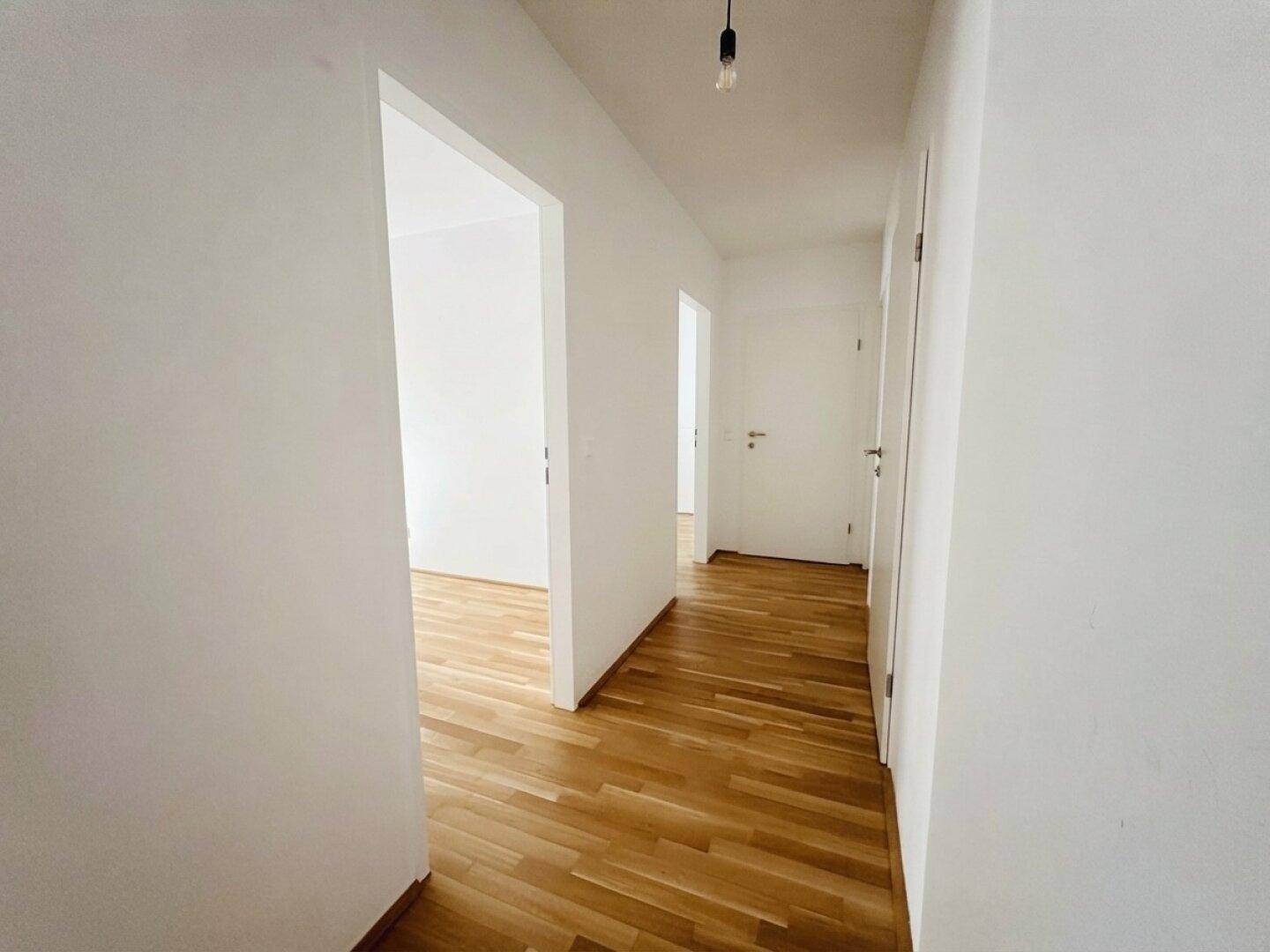 Langer, heller Flur mit Holzboden und mehreren Türen, die zu den angrenzenden Räumen führen.