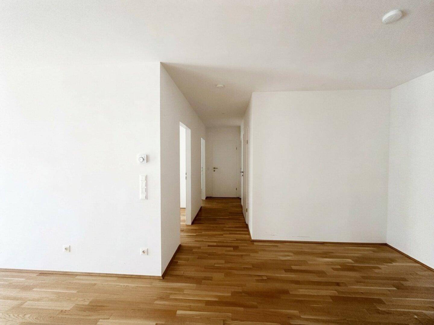 Heller Eingangsbereich mit Holzboden und weißen Wänden, der zu weiteren Räumen führt.