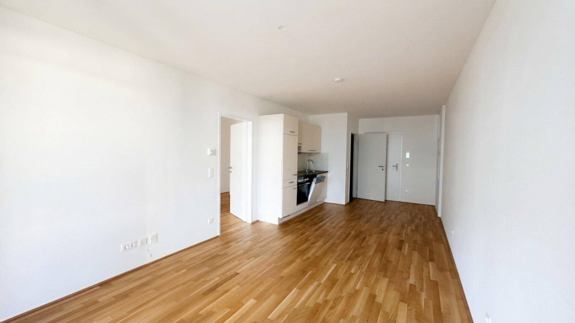 Geräumiger, offener Wohnbereich mit integrierter Küchenzeile und hellem Parkettboden.
