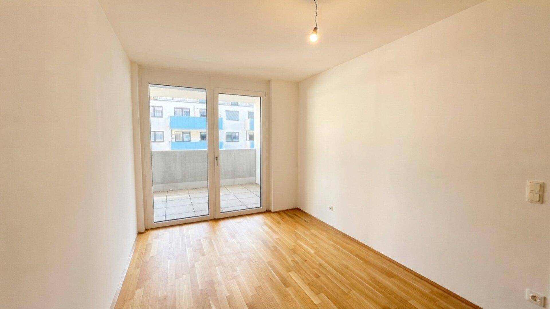 Helles Schlafzimmer mit Parkettboden und großem Fenster, das Zugang zum Balkon bietet.