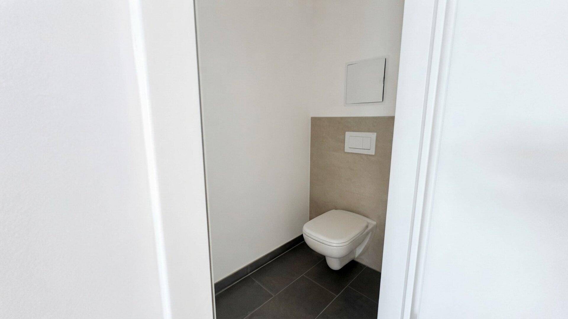 Modernes Gäste-WC mit wandhängender Toilette und dunklen Bodenfliesen.
