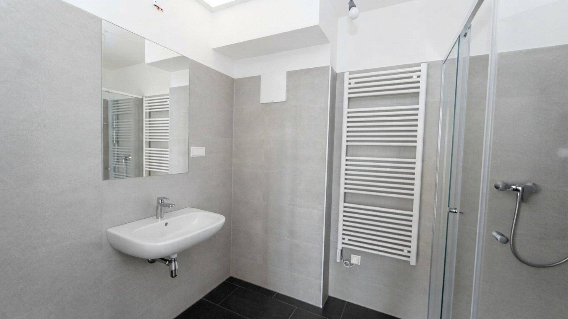 Helles Badezimmer mit Waschbecken, großem Spiegel, Duschkabine und Handtuchheizkörper.