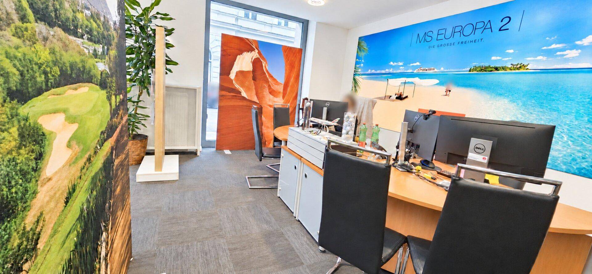 Arbeitsbereich in einem Büro mit Schreibtischen, Computern und großen Landschaftsbildern an den Wänden.