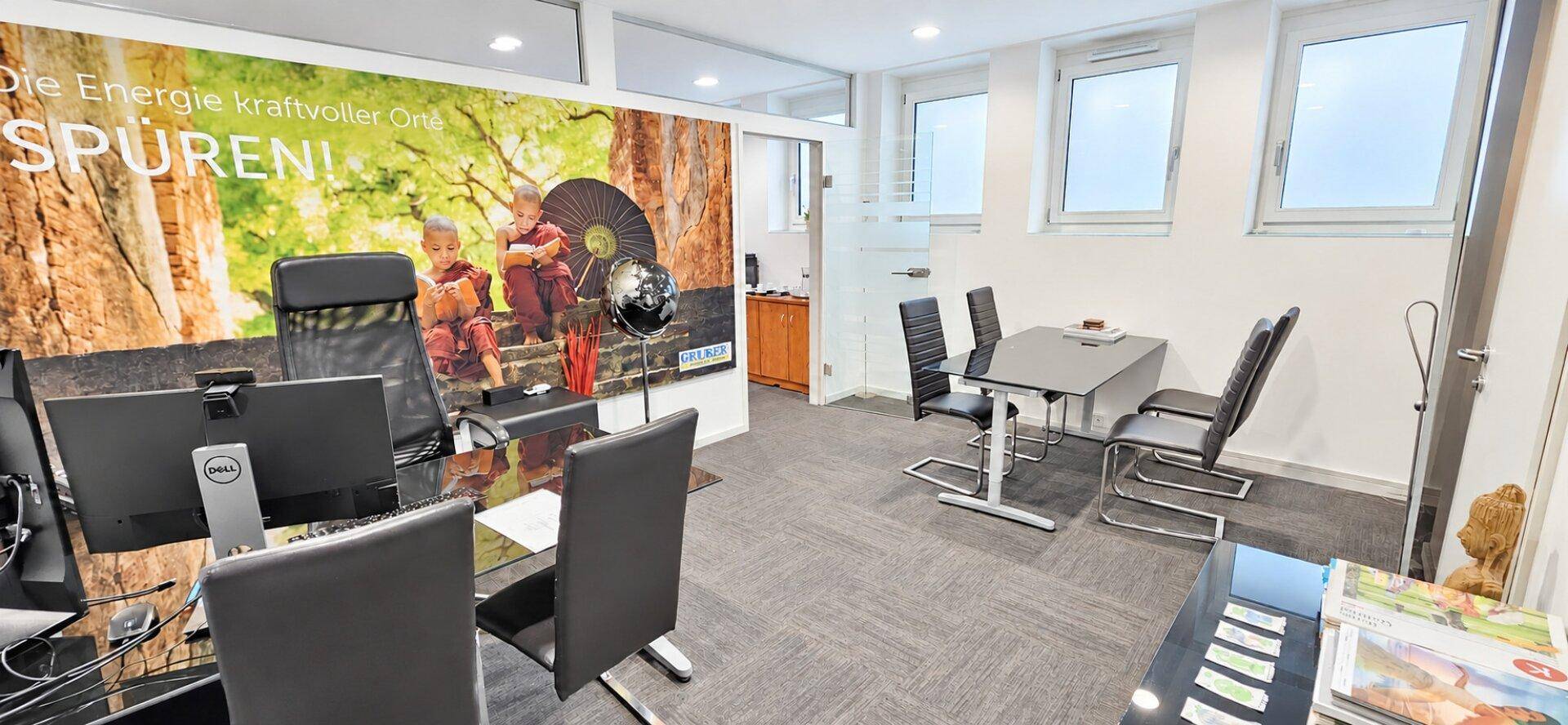 Büro mit Besprechungstisch, Arbeitsplätzen und einer großen Wanddekoration mit Naturmotiven.