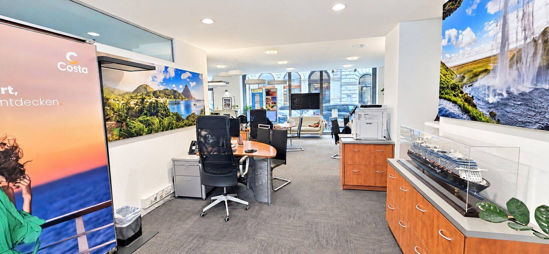 Geräumiges Büro mit mehreren Arbeitsplätzen, einem Schiffsmodell und dekorativen Wandbildern.