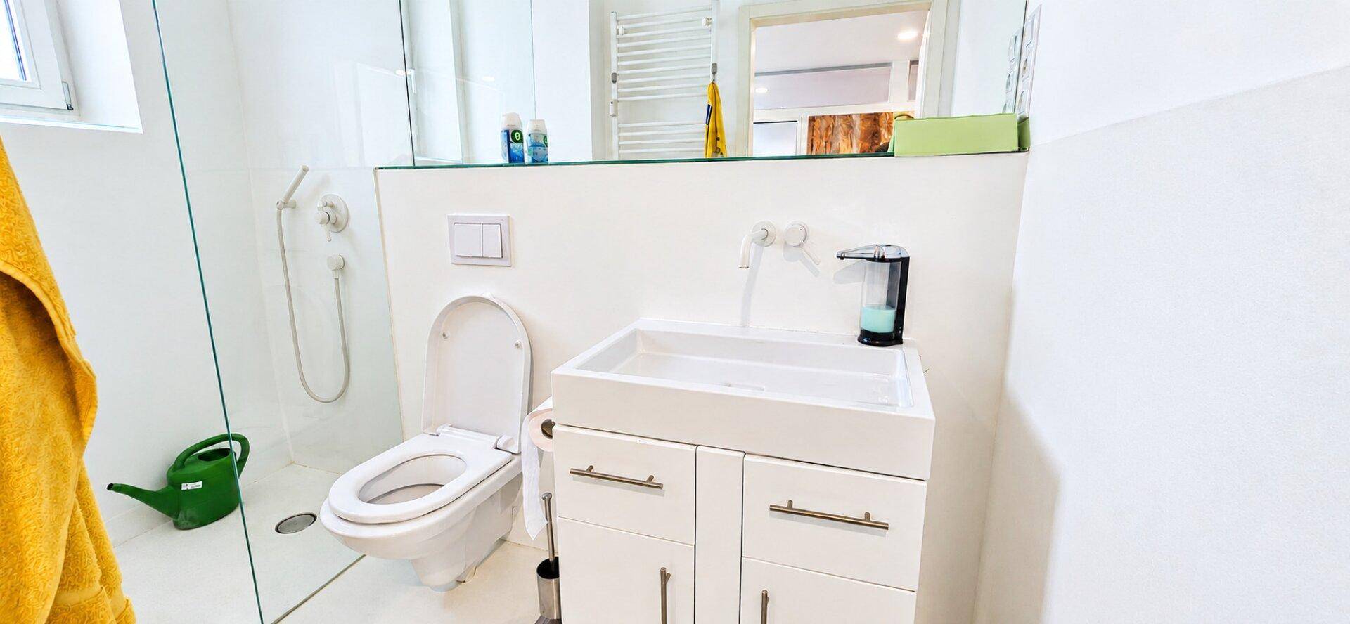 Modernes Badezimmer mit Toilette, Waschbecken und einer Duschkabine, alles in hellen Farben gehalten.