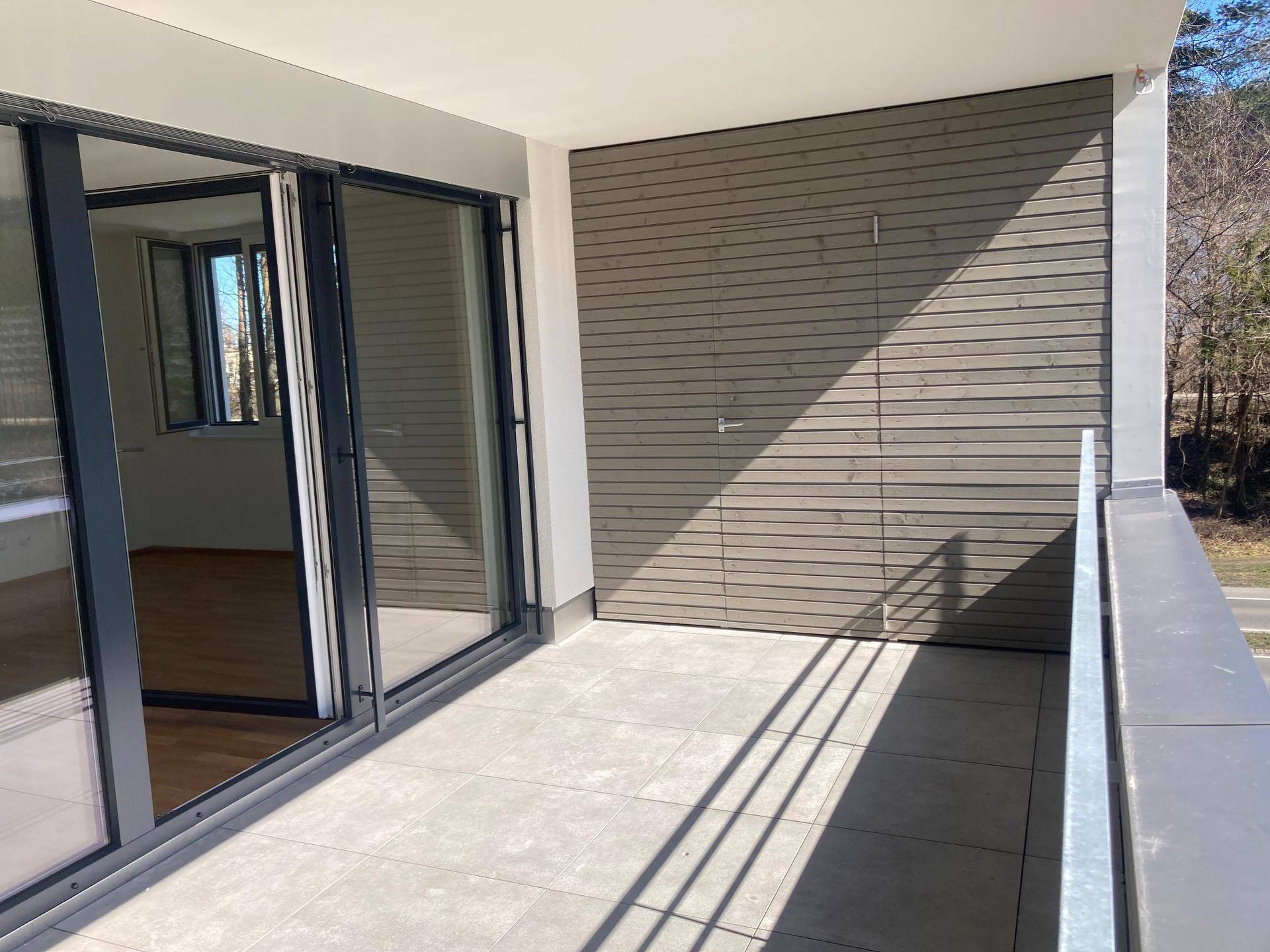 Heller Balkon mit Fliesenboden und Zugang zum Innenbereich, umgeben von Natur.