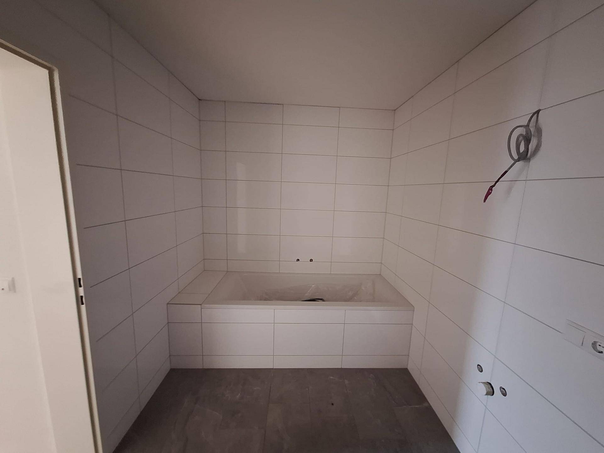 Modern gefliestes Badezimmer mit eingebauter Badewanne, bereit für die Endmontage.