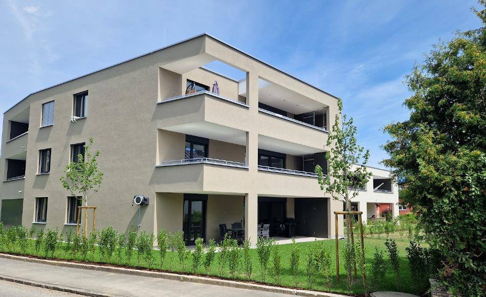 Neubau-Mehrfamilienhaus mit modernen Balkonen und einer möblierten Terrasse im Erdgeschoss.