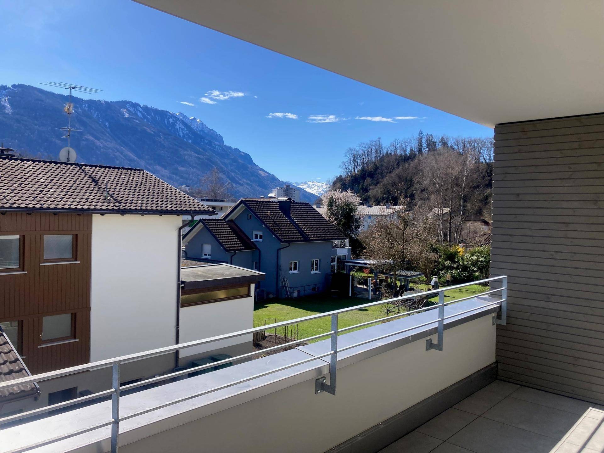 Geräumiger Balkon mit Bergblick und umliegender Wohnbebauung unter blauem Himmel.