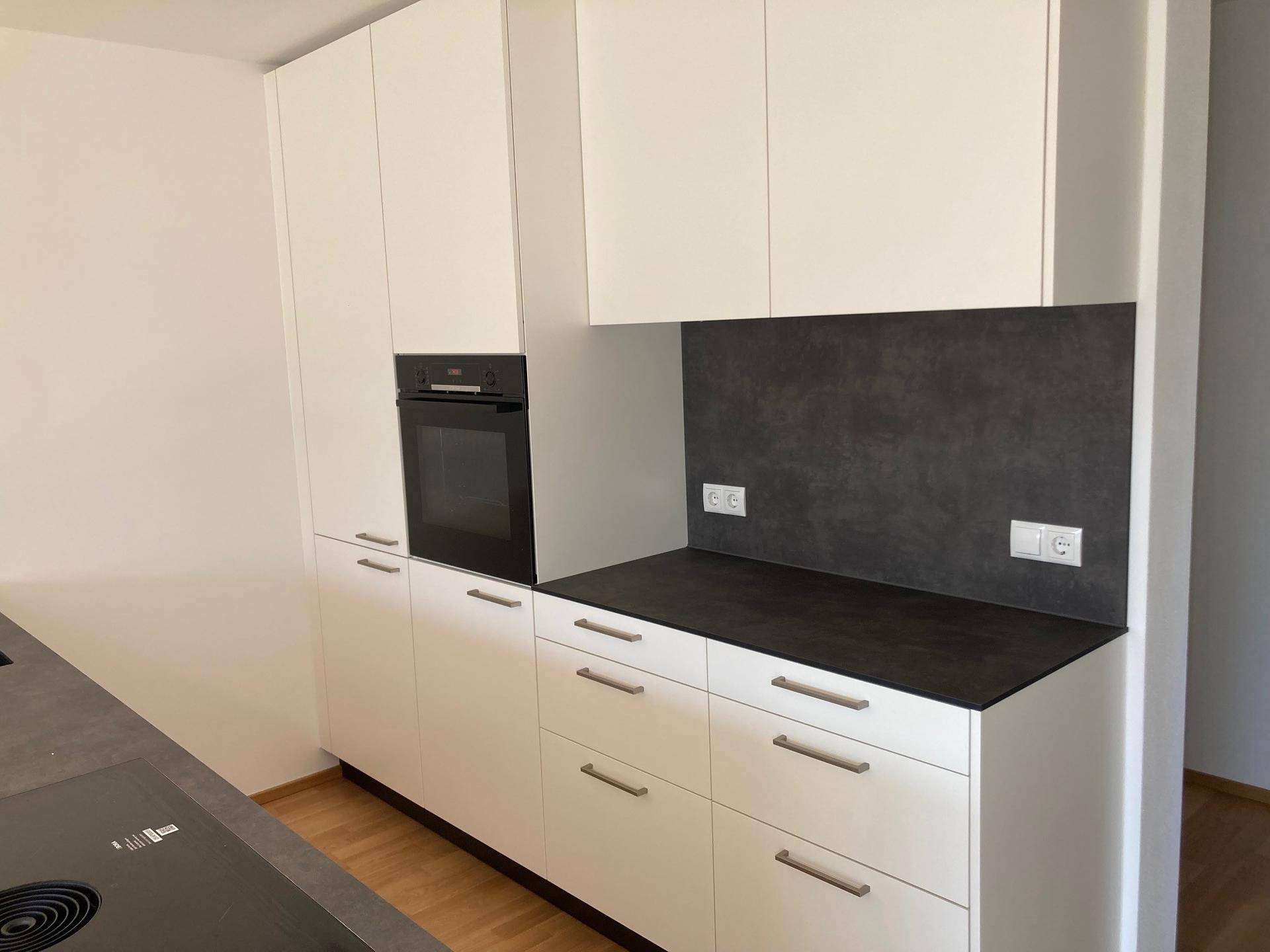 Detailansicht der modernen Einbauküche mit integriertem Backofen und weißen Schränken.