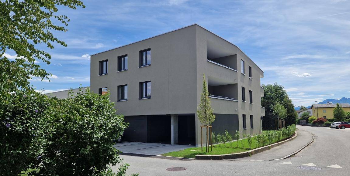 Modernes Mehrfamilienhaus mit schlichter Fassade und integrierten Balkonen in grüner Umgebung.