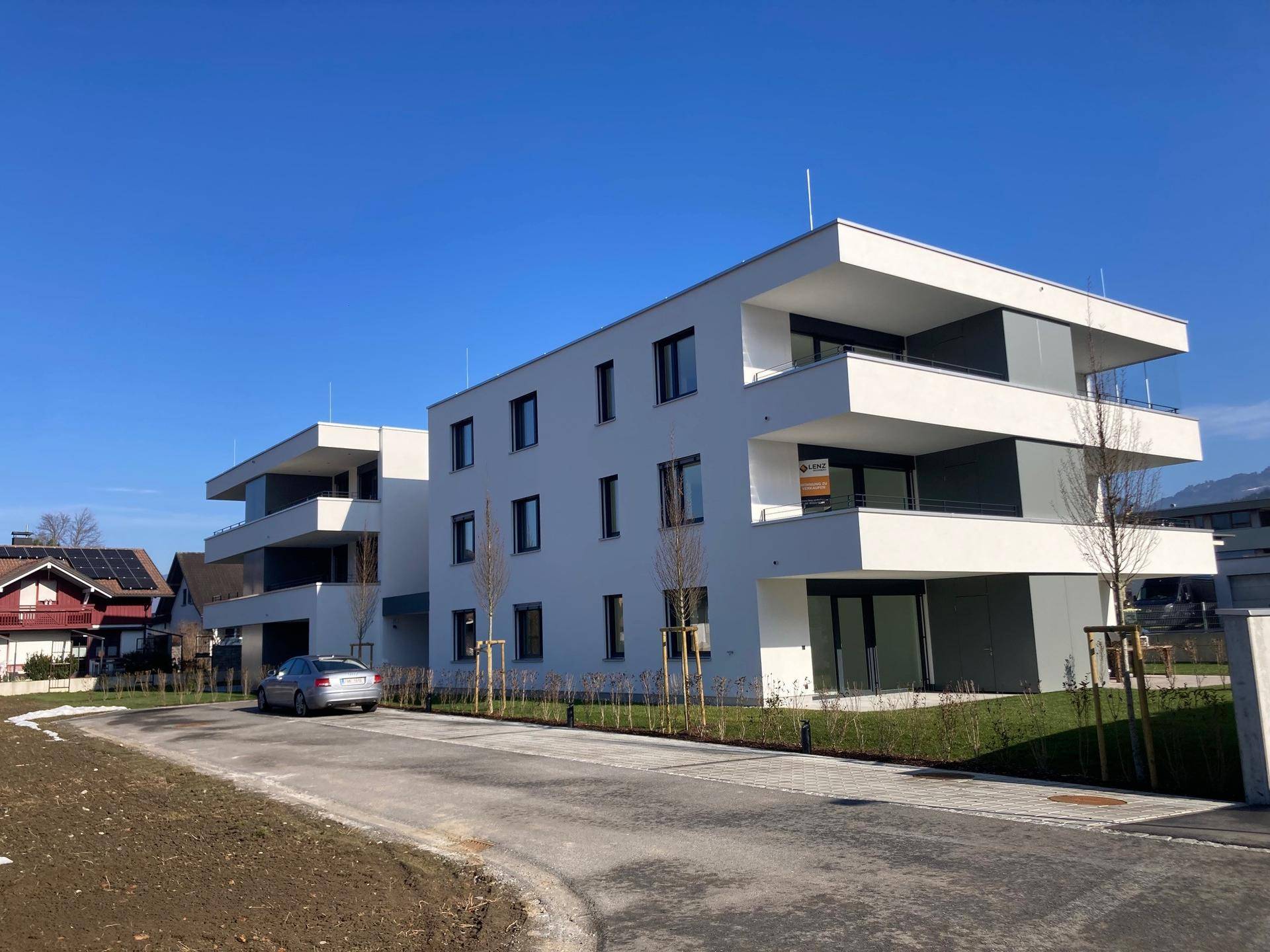 Moderne Wohngebäude mit Balkonen und großen Fensterfronten entlang einer Zufahrtsstraße in sonniger Lage.