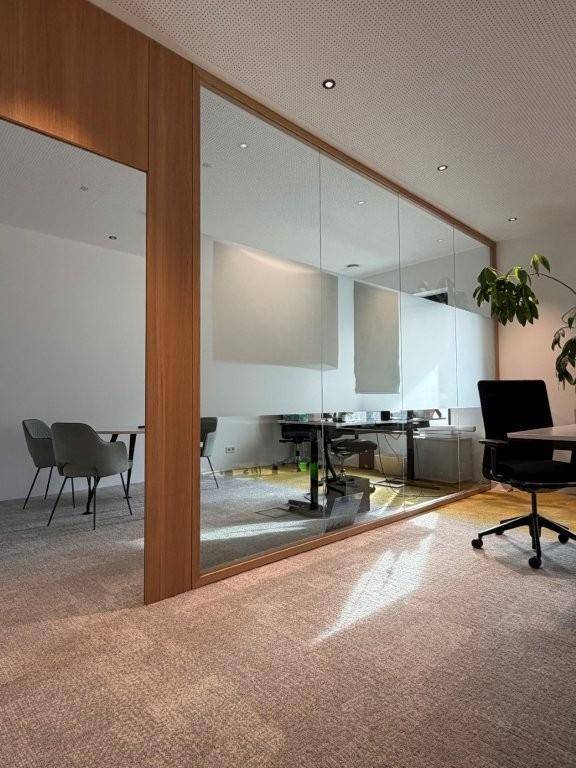 Modernes Büro mit Glaswänden, Holzelementen und Teppichboden, das viel Tageslicht hereinlässt.