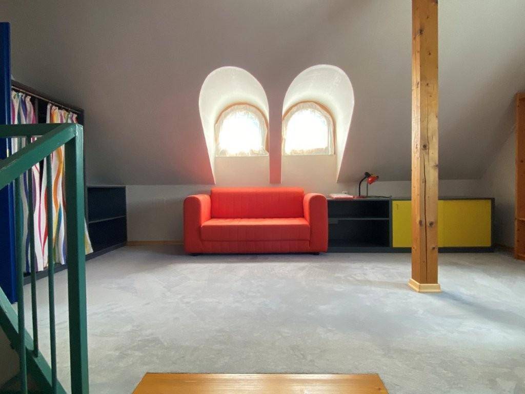 Gemütlicher Dachbodenraum mit rotem Sofa, Teppichboden und zwei charmanten Bogenfenstern.
