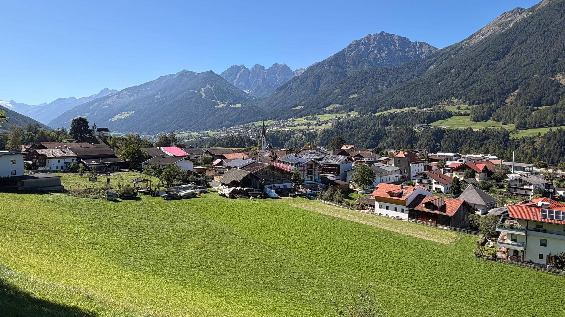 Weitläufiger Blick auf ein charmantes Dorf im Tal, eingebettet in eine beeindruckende Bergkulisse.