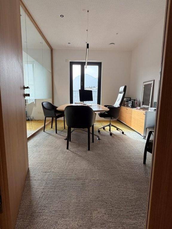 Elegantes Einzelbüro mit Holztür, Glaswand, Schreibtisch und Blick auf die Berge durch die Tür.
