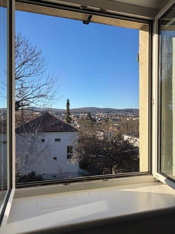 Klarer Ausblick aus dem Fenster über die Dächer der Stadt und die umliegende Landschaft.