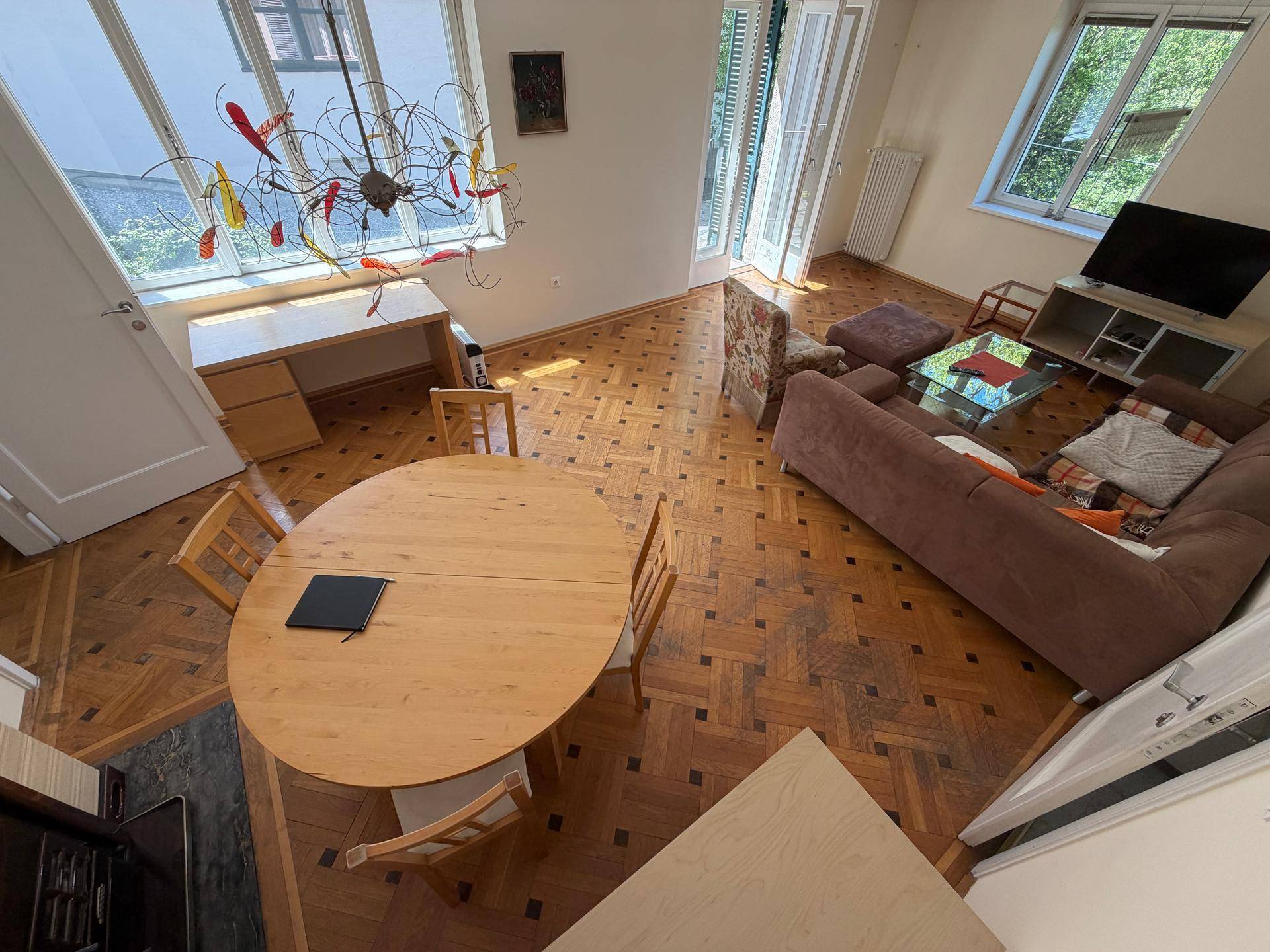 Geräumiger Wohn- und Essbereich mit Holzboden, großem Esstisch und moderner Deckenleuchte.