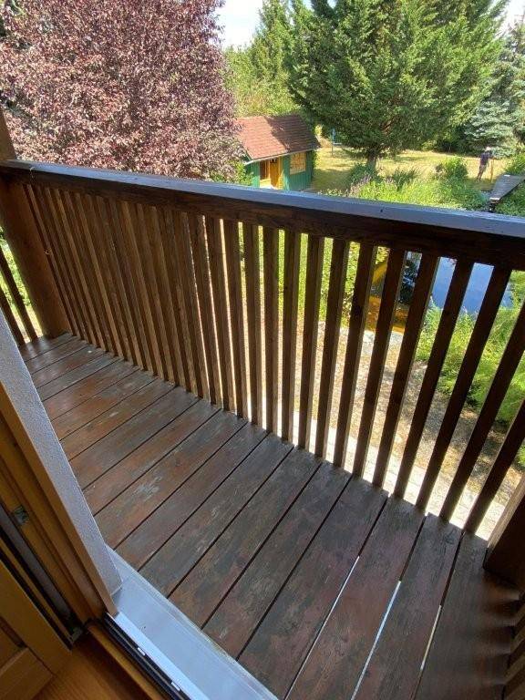 Holzbalkon mit Blick auf den grünen Garten und ein kleines Gartenhaus im Hintergrund.