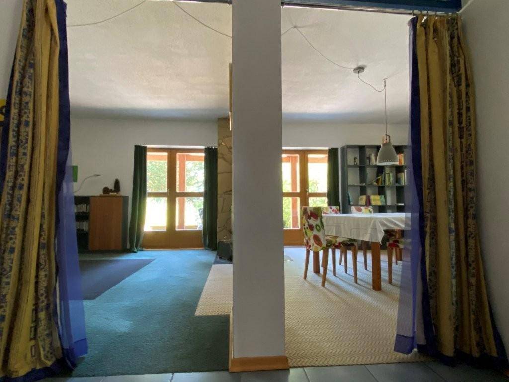 Wohn- und Essbereich mit farbigen Vorhängen, Teppichboden und einem Esstisch mit bunten Stühlen.