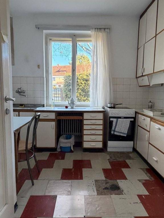 Einfache Küche mit Fliesenboden, weißer Einrichtung und Blick ins Grüne durch das Fenster.