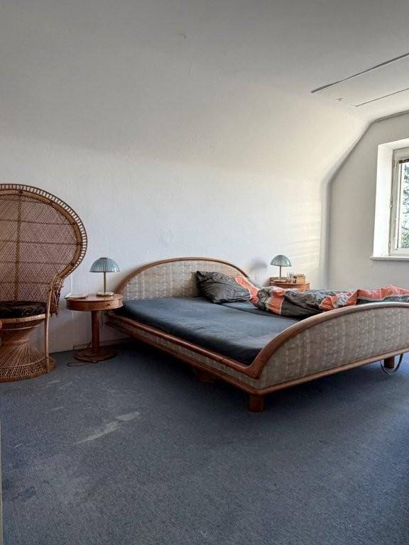 Schlafzimmer im Dachgeschoss mit schrägen Wänden, Teppichboden und Rattanmöbeln.