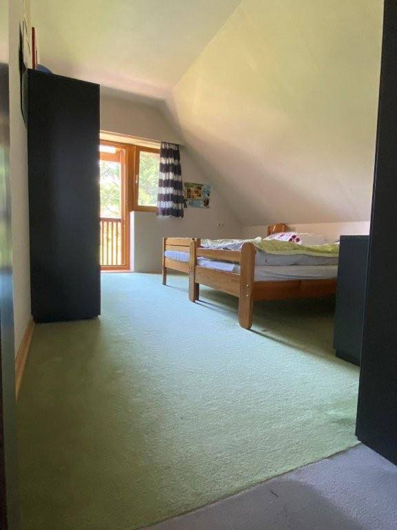 Schlafzimmer im Dachgeschoss mit grünem Teppichboden, Holzbett und Zugang zu einem Balkon.