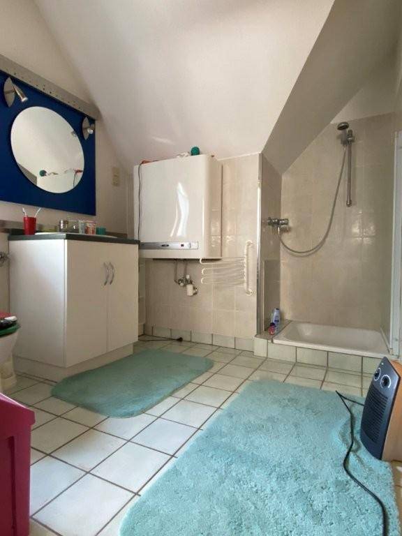 Badezimmer mit Duschbereich, Fliesenboden und einem Warmwasserbereiter an der Wand.