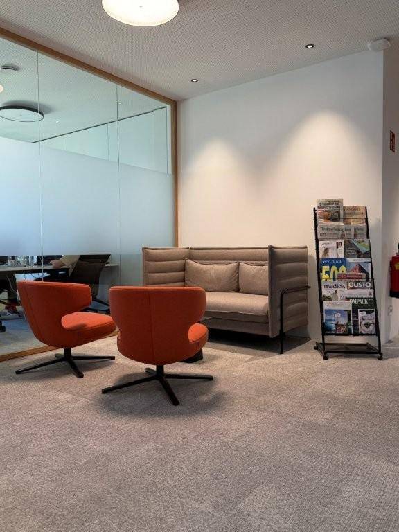 Gemütlicher Loungebereich mit bequemen Sesseln, Sofa und einem Zeitschriftenständer in einem modernen Büro.